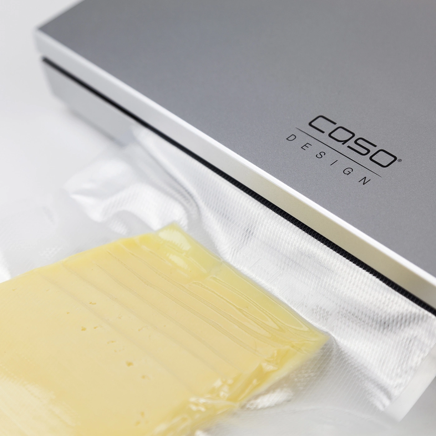 Cheese in plastic packaging next to a vacuum sealer with Caso Design logo.