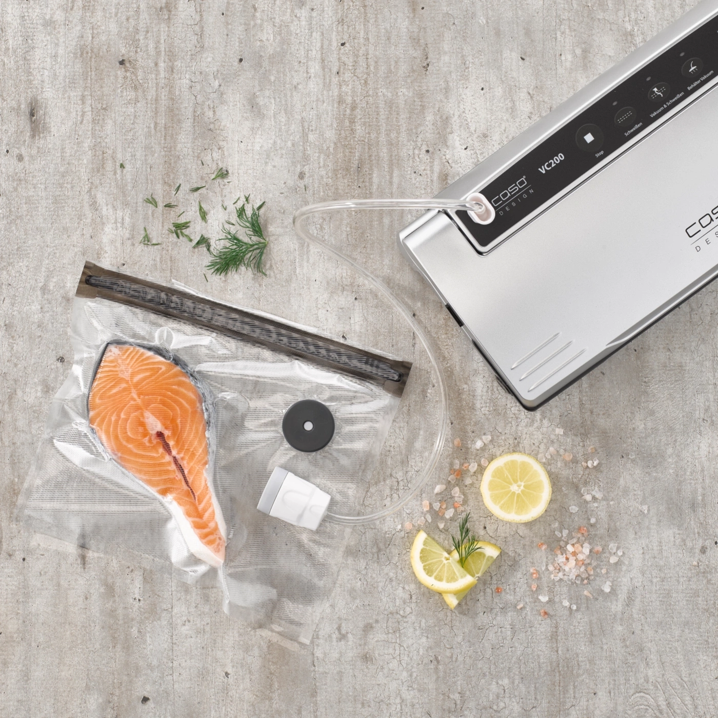 Salmon fillet being vacuum packed, decorated with lemon and herbs, next to a vacuum sealer.