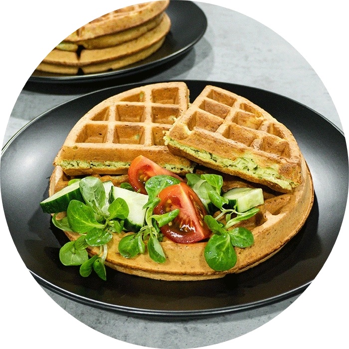 Waffeln mit Salat und Tomaten auf einem schwarzen Teller