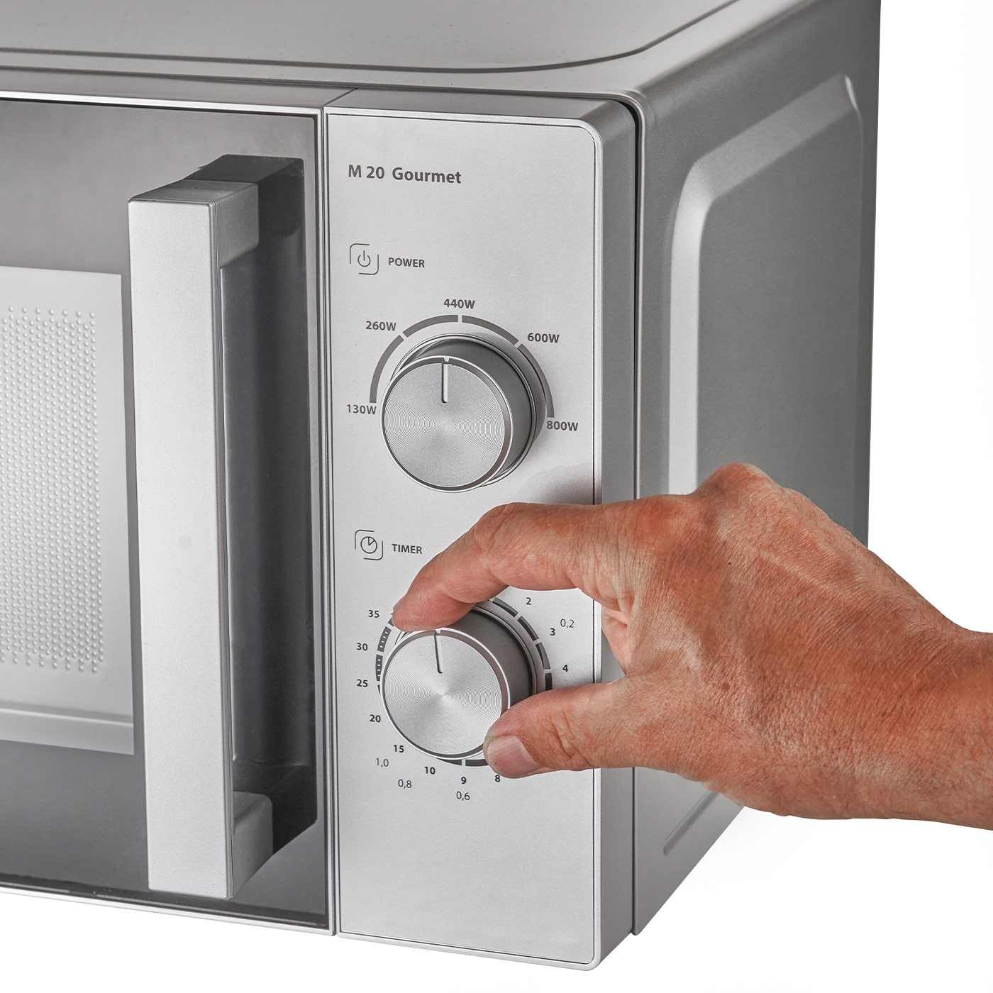 Mikrowelle mit Bedienelementen, Hand dreht den Timer, graue Oberfläche, M 20 Gourmet.