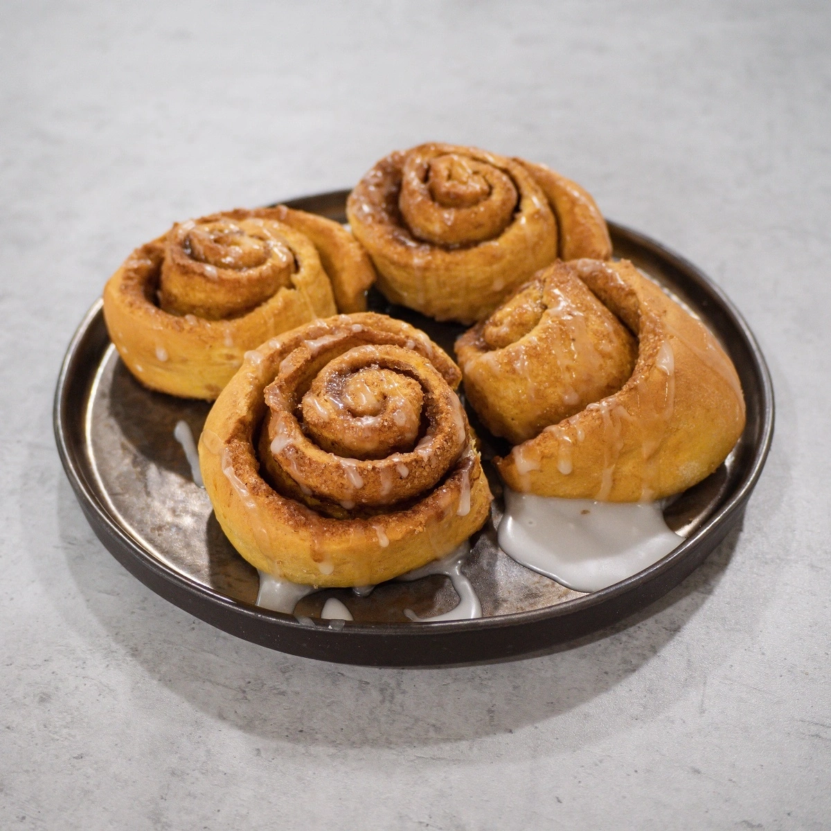 Close-up of four cinnamon rolls on a plate with icing dripping down.