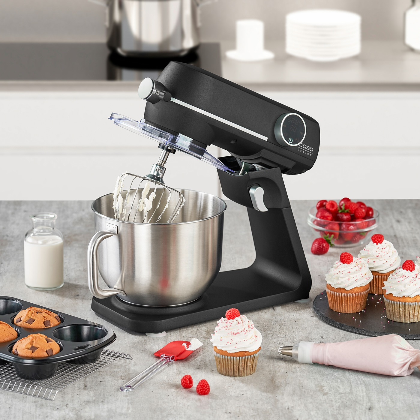 Küchenmaschine mit Cupcakes, Himbeeren und Backutensilien auf einer Arbeitsplatte