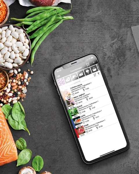 Smartphone mit Essensliste, umgeben von gesunden Lebensmitteln wie Gemüse und Fisch.