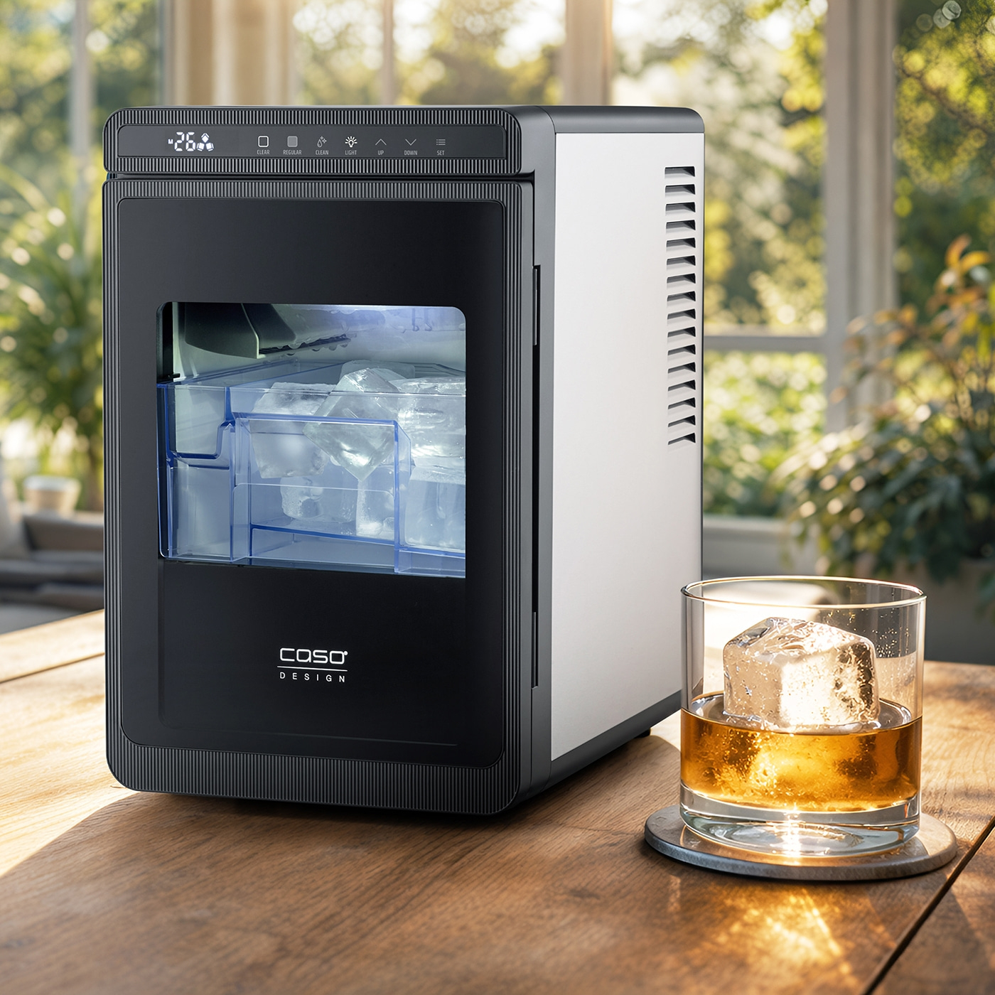 Ein schlanke schwarze Eismaschine steht auf einem Holztisch neben einem Whiskeyglas mit einem großen Eiswürfel.