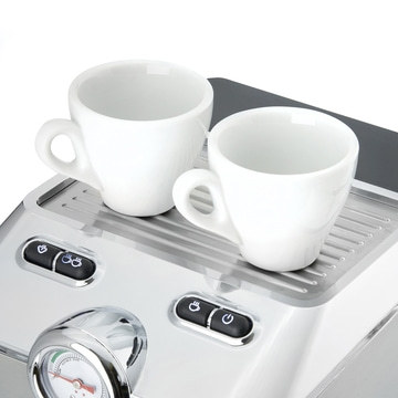 Two white cups on an espresso machine with buttons and a gauge, close-up.