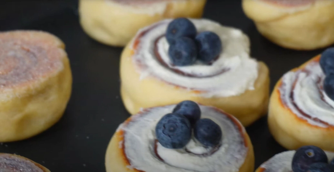 Nahaufnahme von Zimtschnecken mit Blaubeeren und Zuckerguss auf schwarzem Tablett
