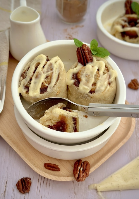 Zimtschnecken mit Pecannüssen und Glasur in einer Schüssel auf einem Holztablett