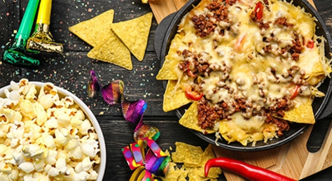 Close-up of nachos with cheese and meat, popcorn, and party decorations on a table.