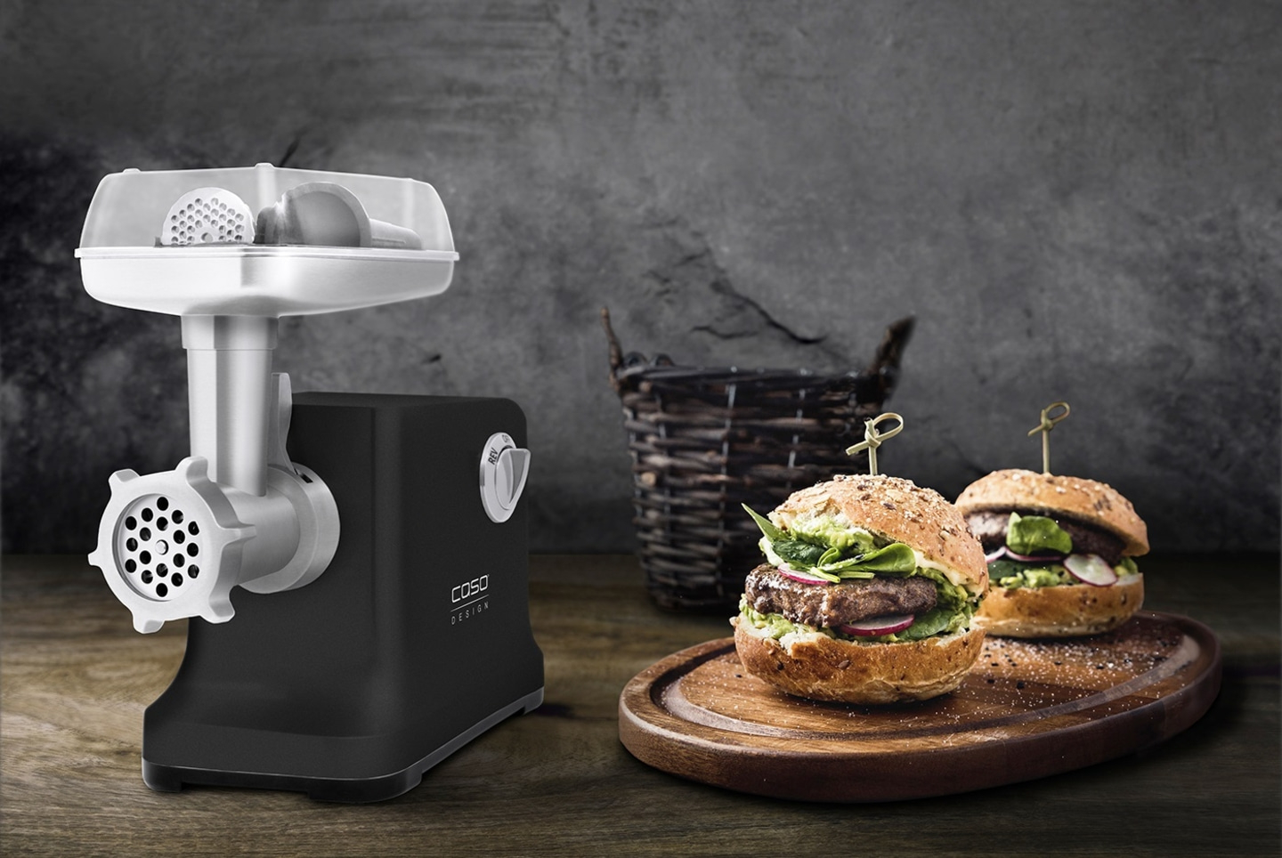 Fleischwolf und Burger auf einem Holzbrett vor grauem Hintergrund