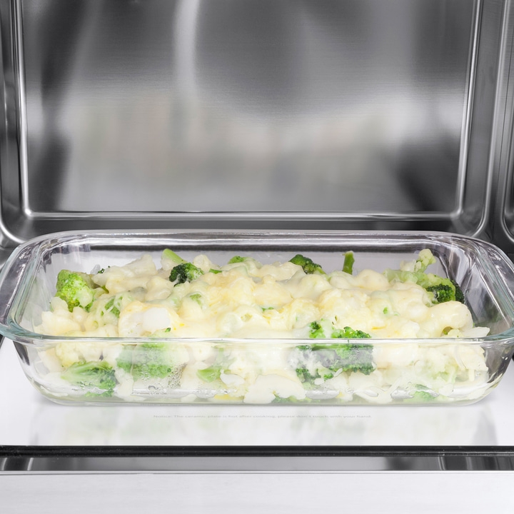 Broccoli casserole in glass dish inside oven. Cheese covers vegetables.