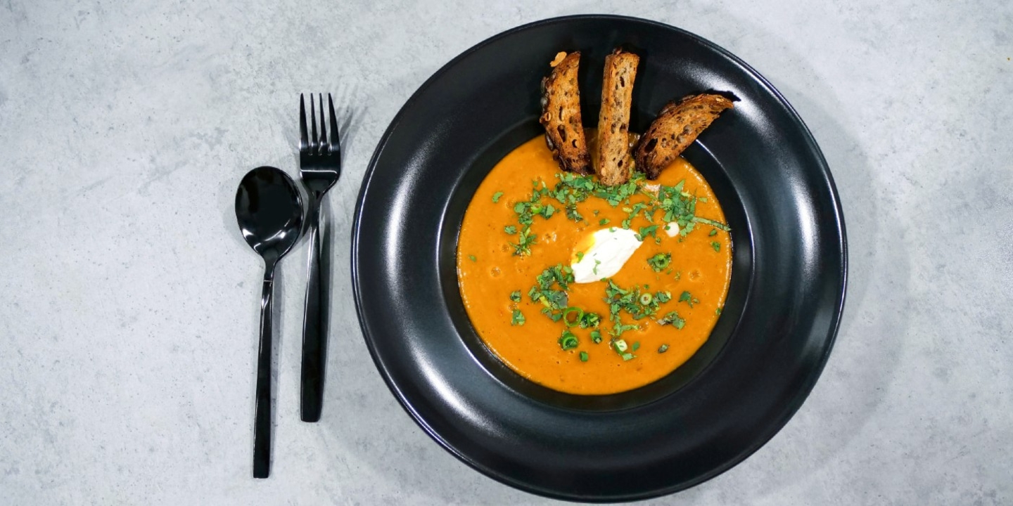 Suppe mit Brot und Löffel und Gabel auf einem schwarzen Teller