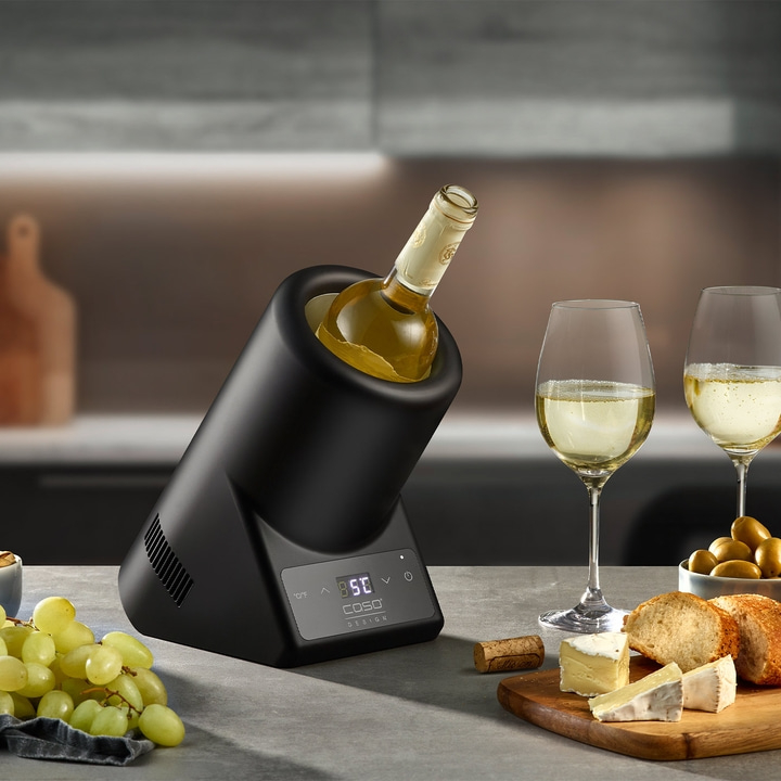 Weinkühler mit Wein, Gläsern, Käse, Brot und Trauben auf einem Tisch.
