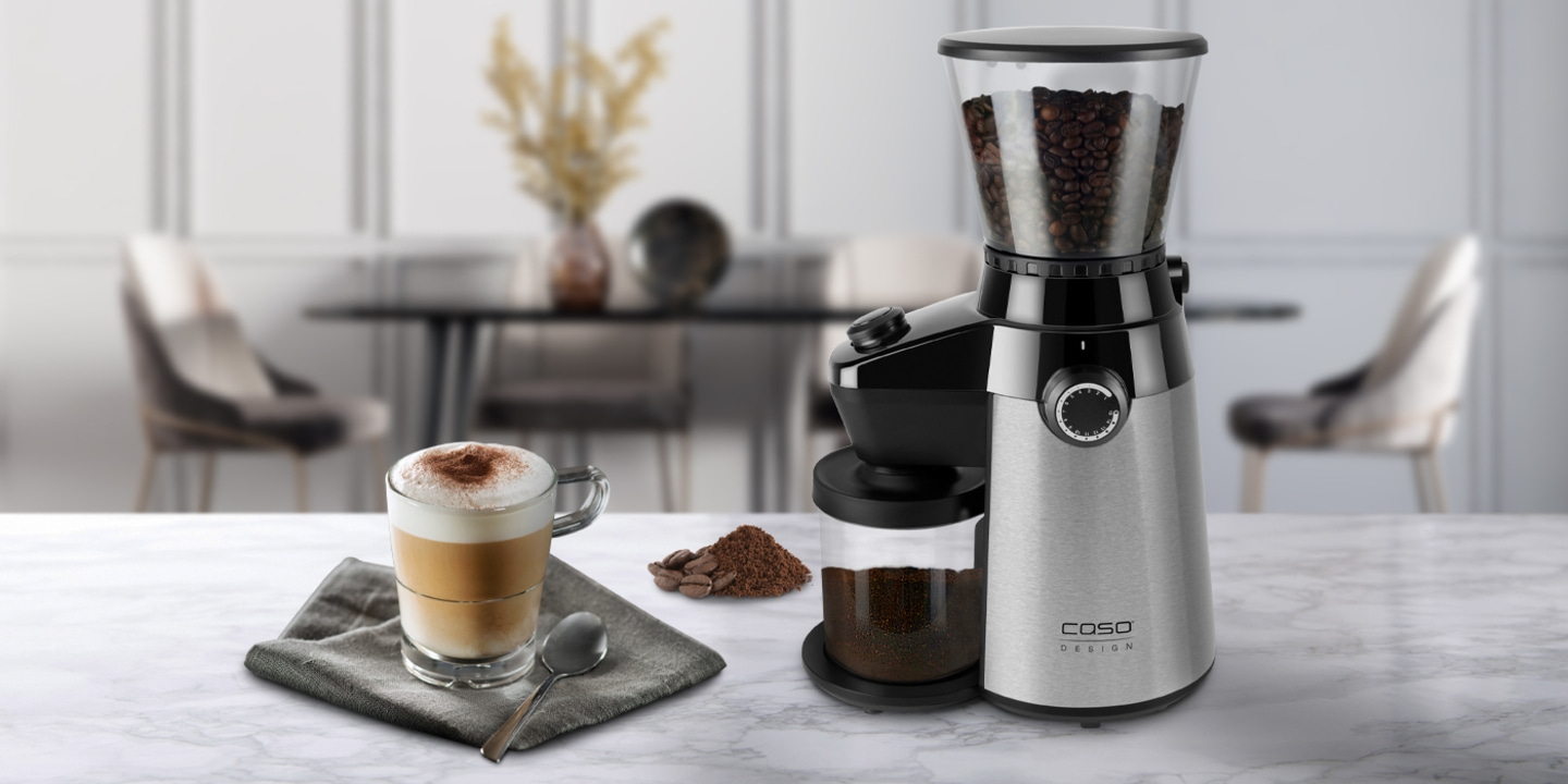 Kaffeemühle mit Kaffeebohnen und Cappuccino auf Marmortisch in Innenraum