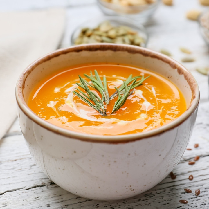 Kürbissuppe mit Rosmarin in einer Schüssel auf einem Holztisch