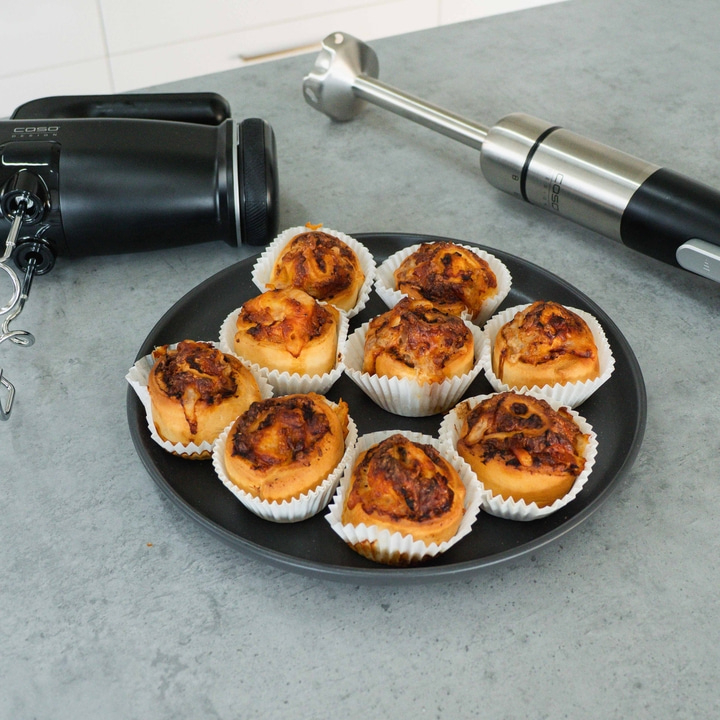 Plate of pastries, a mixer and a stick blender on a gray surface next to it.