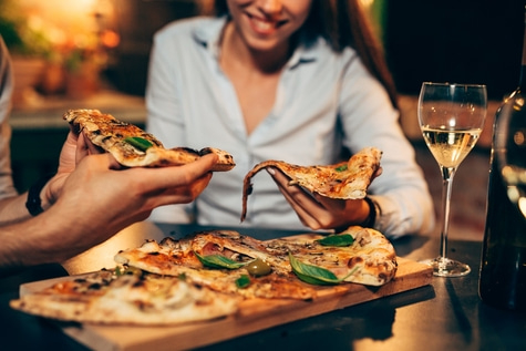 People eating pizza, drinking wine. Close-up of food and drink.