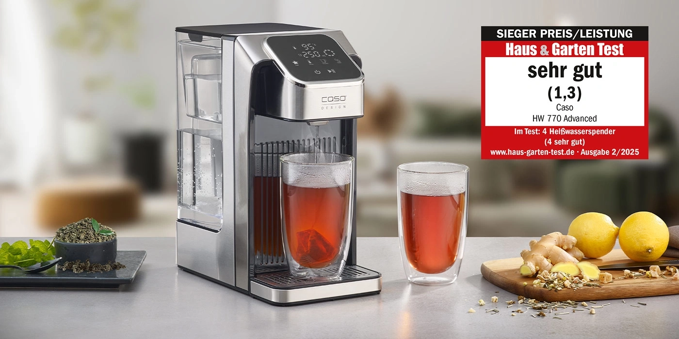 Heißwasserspender mit zwei Gläsern Tee, Zitronen und Ingwer auf einem Tisch.