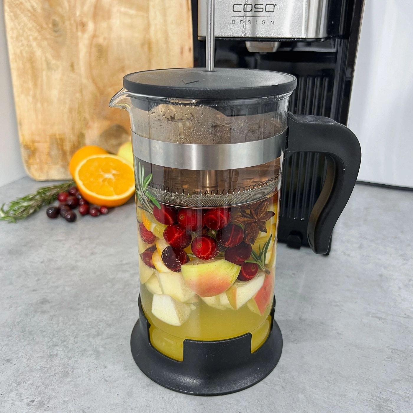 A glass with fruits and herbs, next to a coffee machine, close up shot.