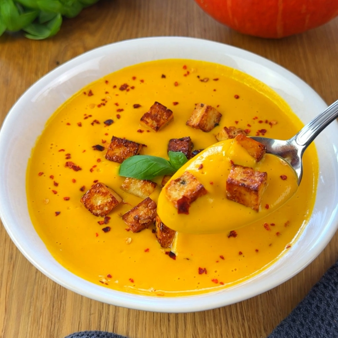 Pumpkin soup with croutons and basil in a white bowl