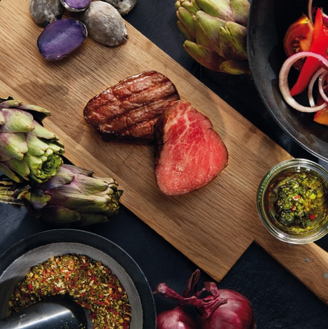 Grilled steak with vegetables and herbs on a wooden board