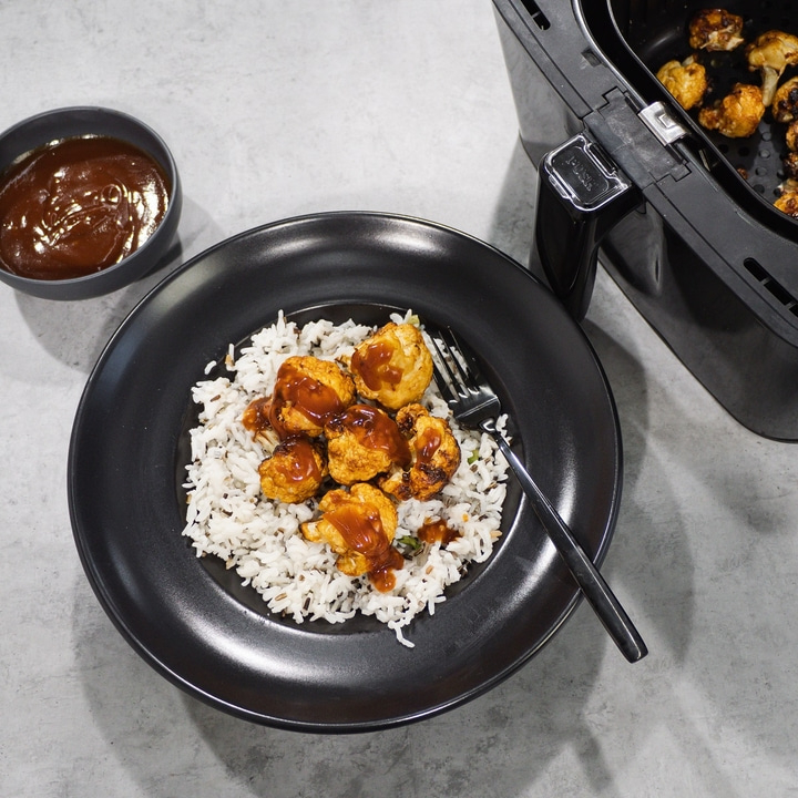 Fried cauliflower with rice and sauce on a black plate with a fork