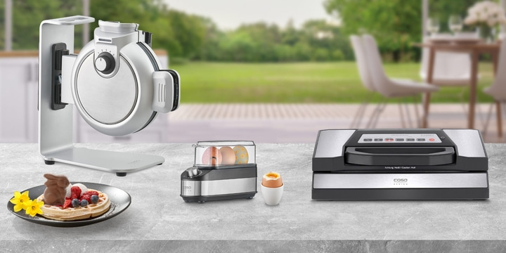 Waffle iron, egg cooker, vacuum sealer and waffle with chocolate bunny on table.