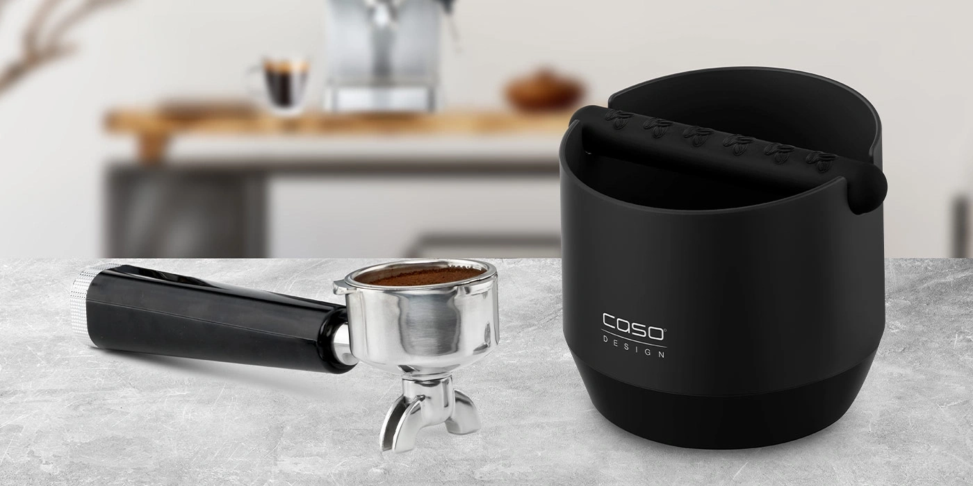 Schwarzer Espresso-Abklopfbehälter mit Siebträger auf grauem Untergrund