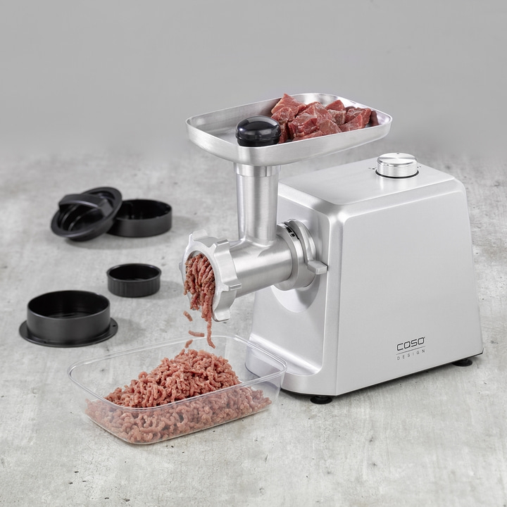 Meat grinder with meat and accessories on gray surface. Caso Design.