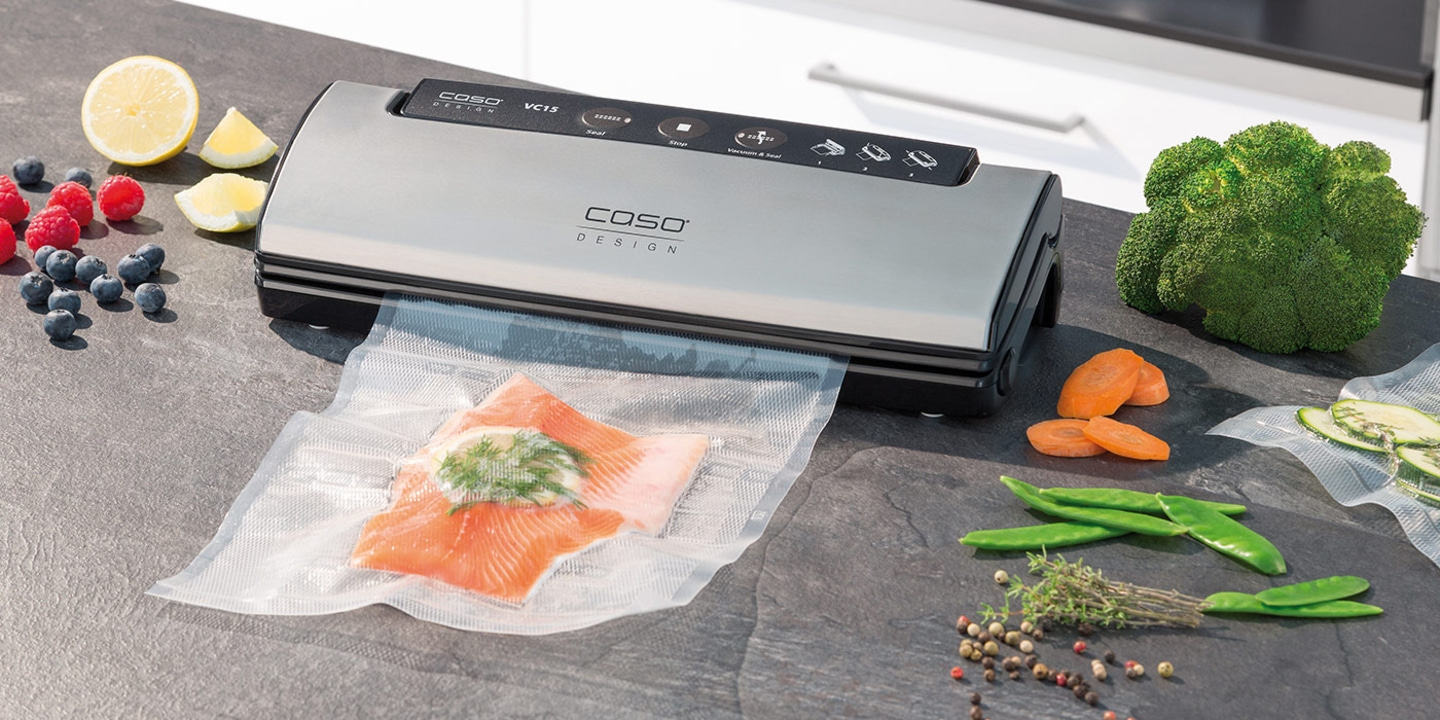 Vacuum sealer with salmon, vegetables, and fruits on a countertop surface.