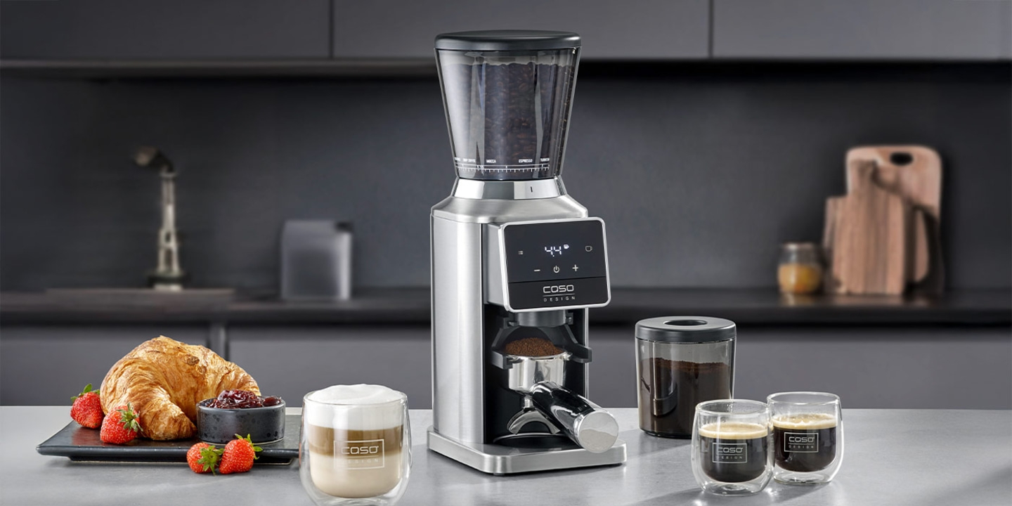 Coffee grinder with breakfast and coffee preparation in the background