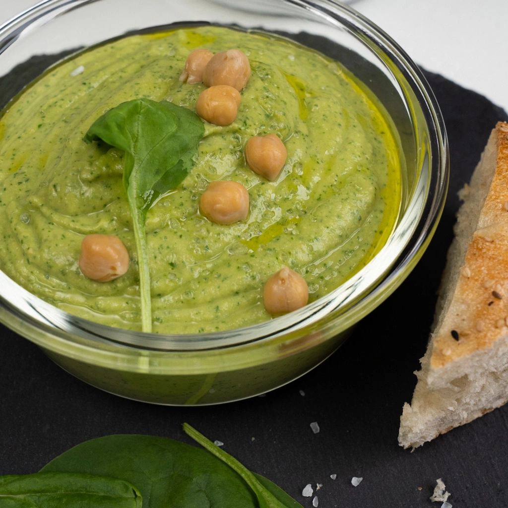 Green dip with chickpeas, spinach, and bread on a black surface