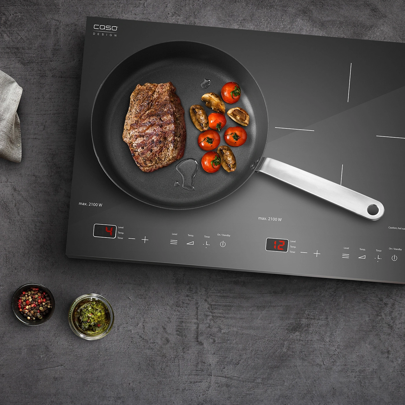 Induktionskochfeld mit Steak, Tomaten und Kräutern, bereit zum Kochen.