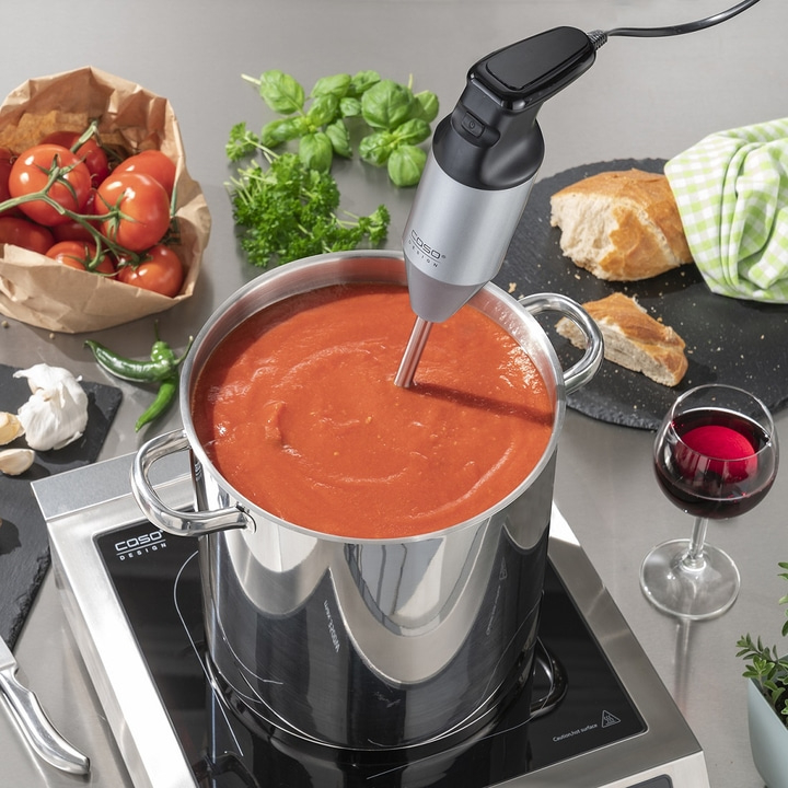 Ein Kochtopf mit Tomatensuppe, Pürierstab, Zutaten und Wein.