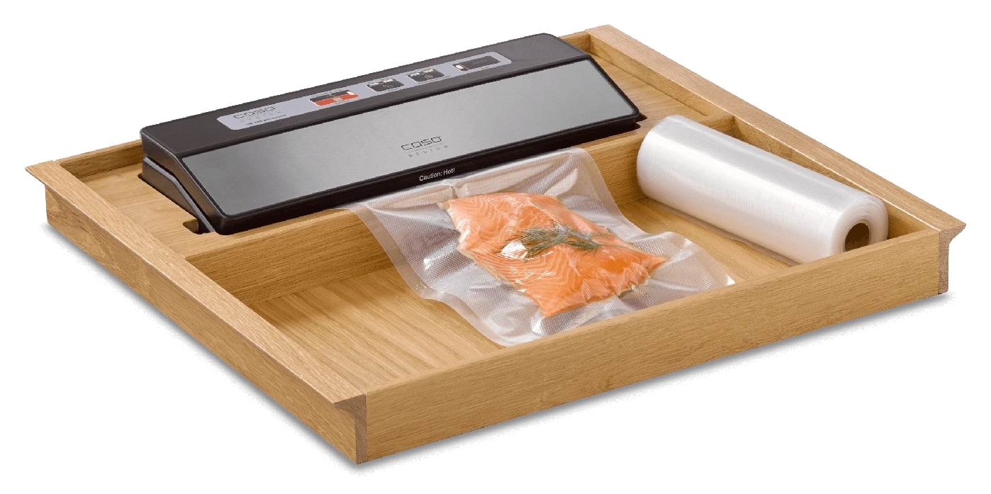 A vacuum sealer with salmon and a roll of film in a wooden drawer.