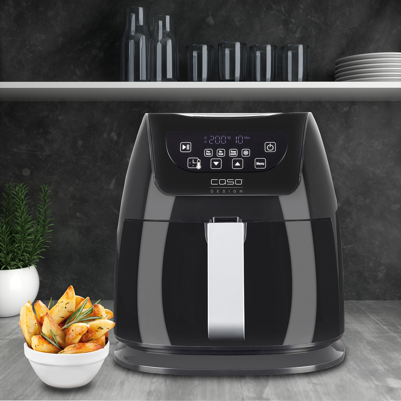 Black air fryer with fries in a bowl on a table with a plant.
