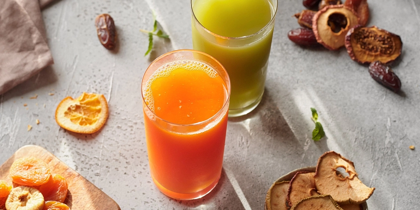 Two glasses of juice with dried fruits and orange slices.