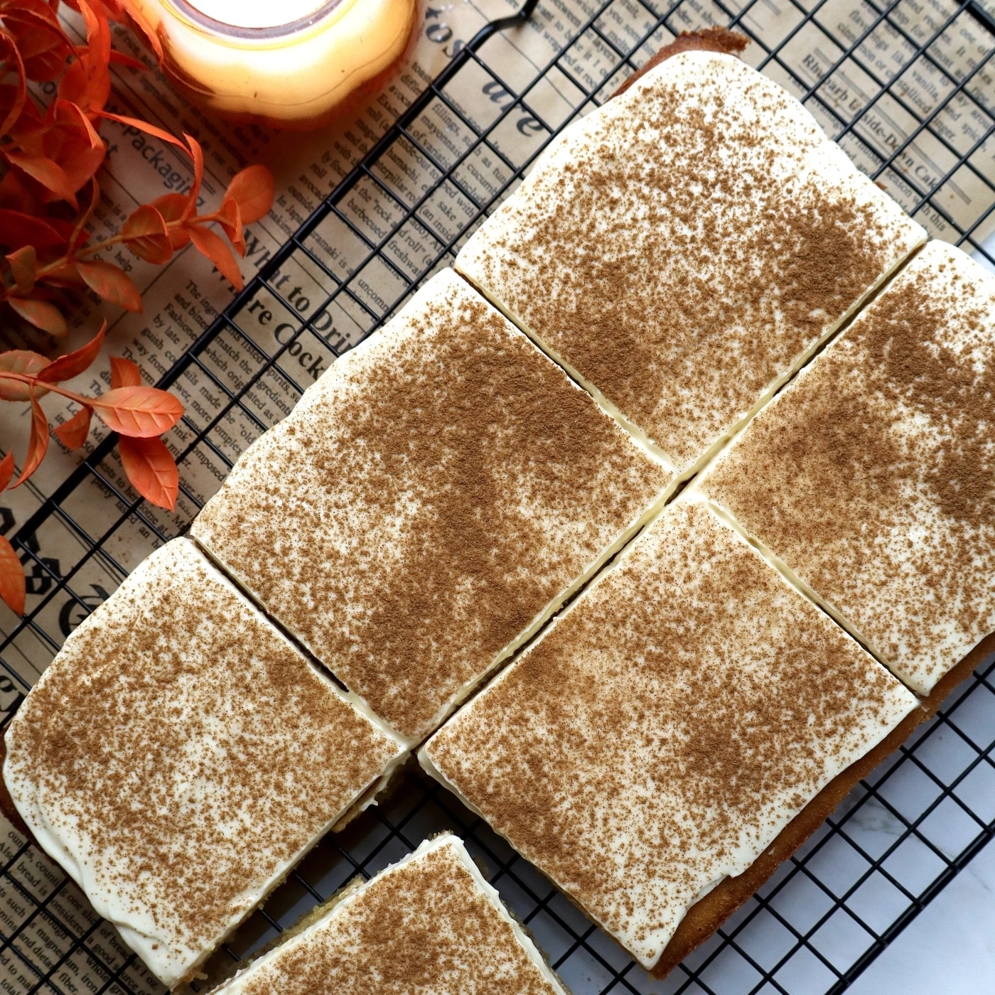 A cake with white frosting and cinnamon sprinkled on top, on a cooling rack.