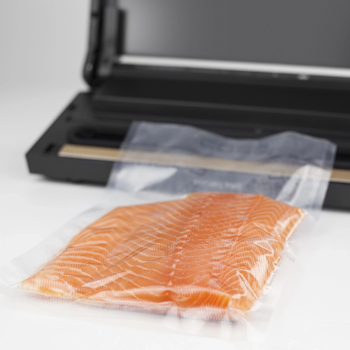 Salmon fillet in vacuum packaging in front of a vacuum sealer on white background