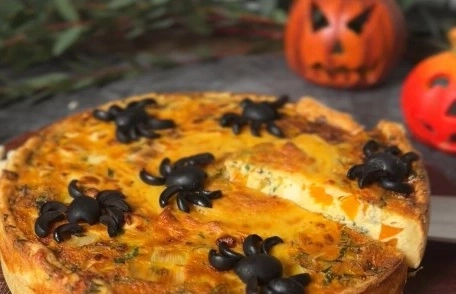 Halloween-Kuchen mit Spinnen-Dekoration und Kürbis-Dekoration im Hintergrund