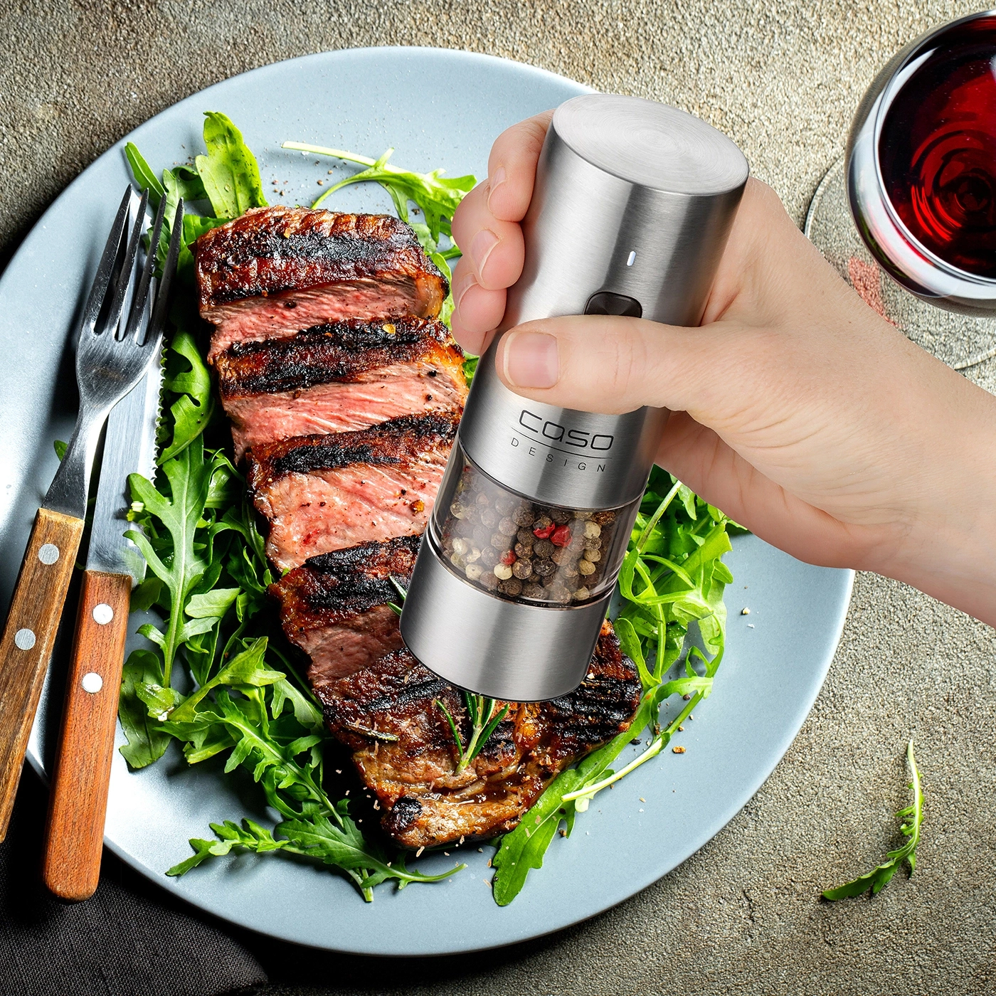 Elegant steak with arugula and a spice grinder, plus a glass of red wine.
