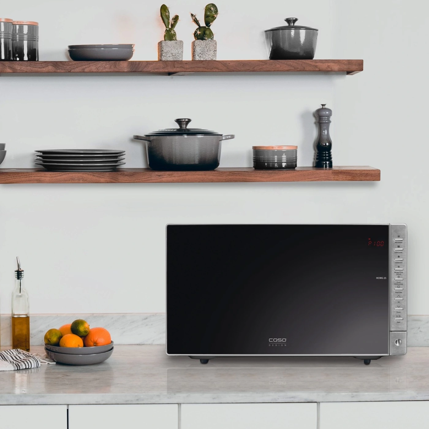 Microwave in kitchen with fruit, plates, and decor on shelves.