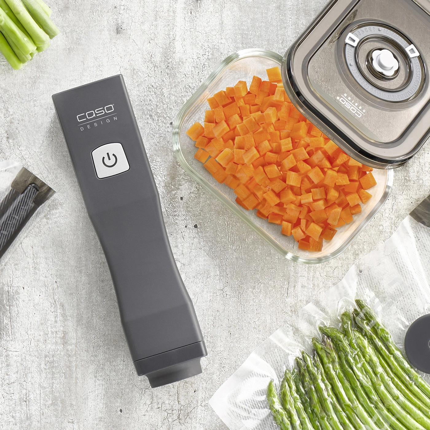 Vegetables, vacuum sealer and container on gray background. Carrots and asparagus.