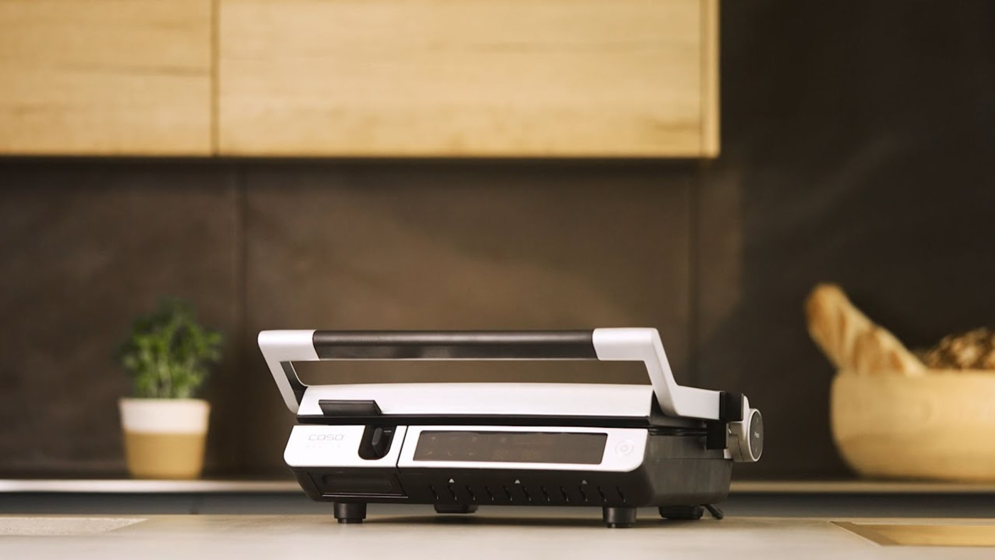 An open contact grill in a kitchen with bread and a plant pot.