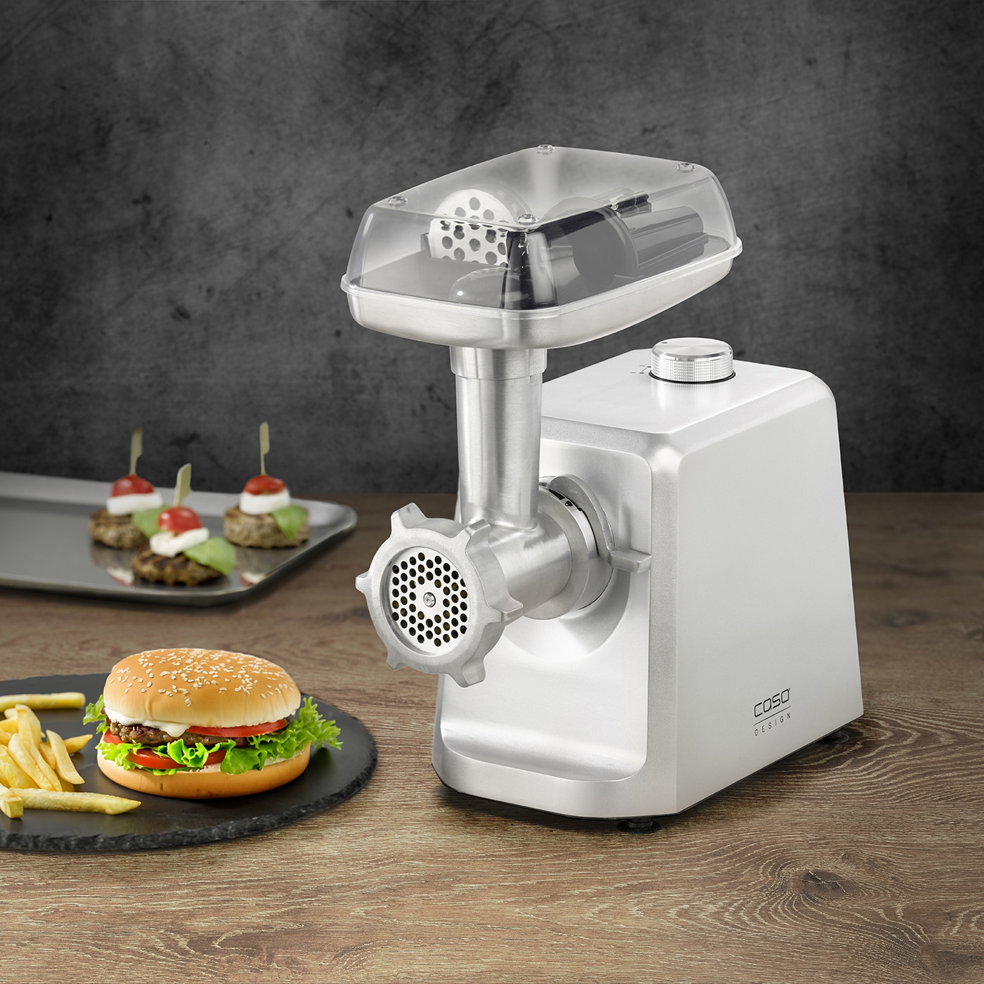Meat grinder with burger and snacks on a wooden table against a dark background