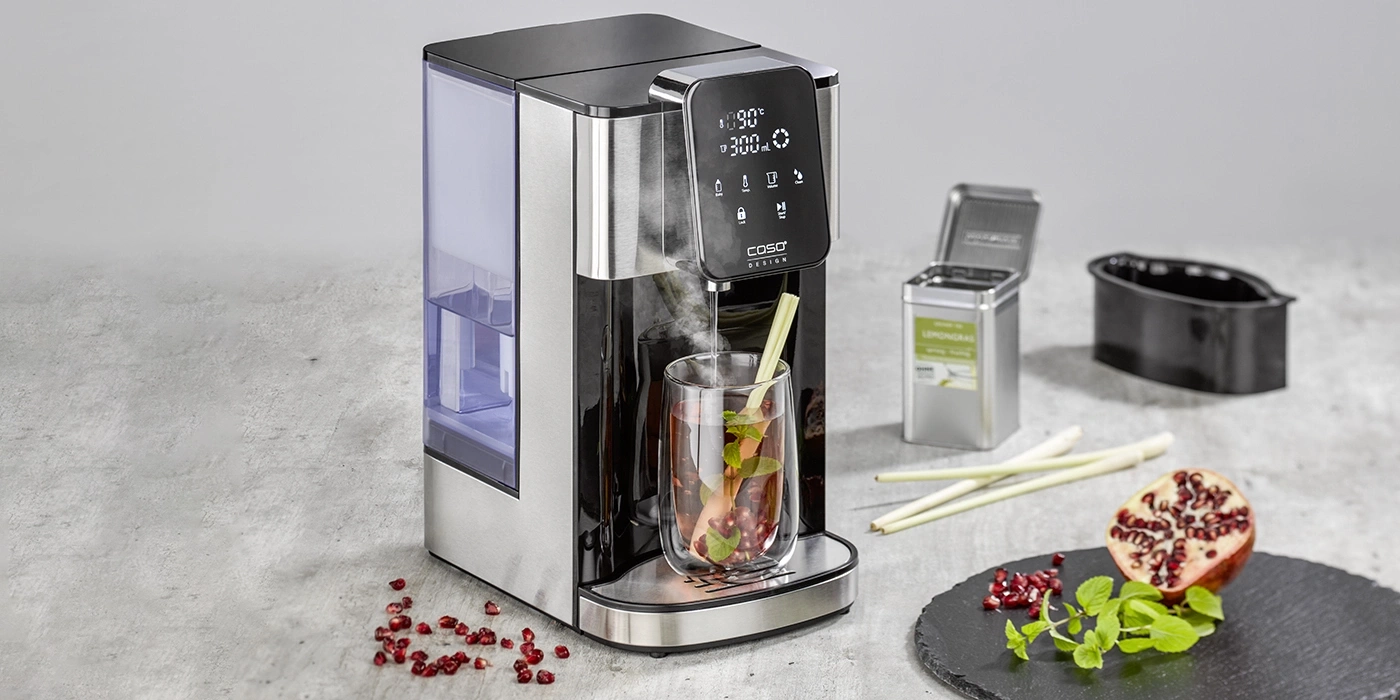 Teemaschine mit Glas, Lemongras, Granatapfel und Kräutern auf einem Steinbrett