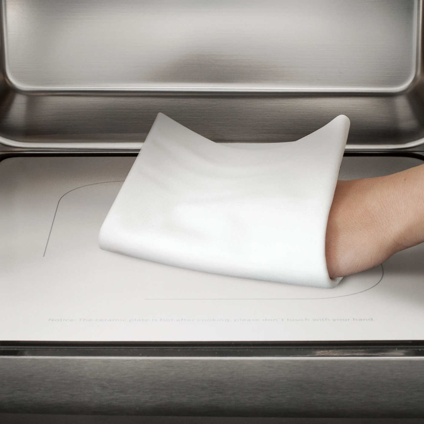 Hand touching hot ceramic plate. Warning: Don't touch! Oven, white cloth, caution.