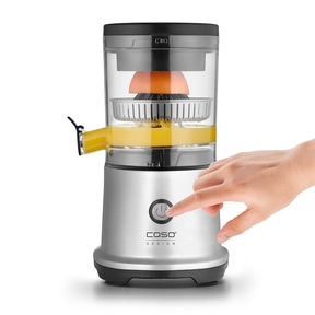 Ein Finger drückt den Ein-Schalter eines Entsafters, der Orangensaft produziert.