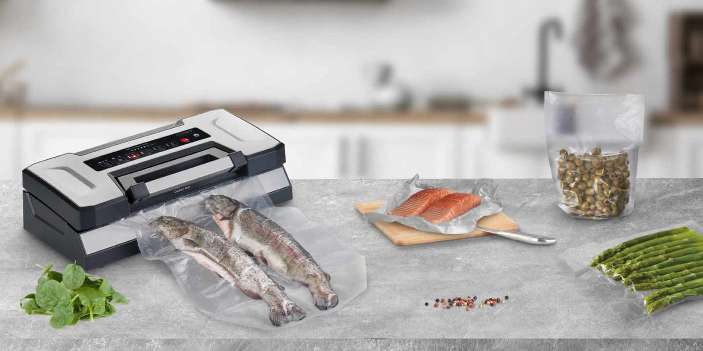 Vakuumiergerät mit Fisch, Lachs, Gemüse und Gewürzen auf einem Tisch