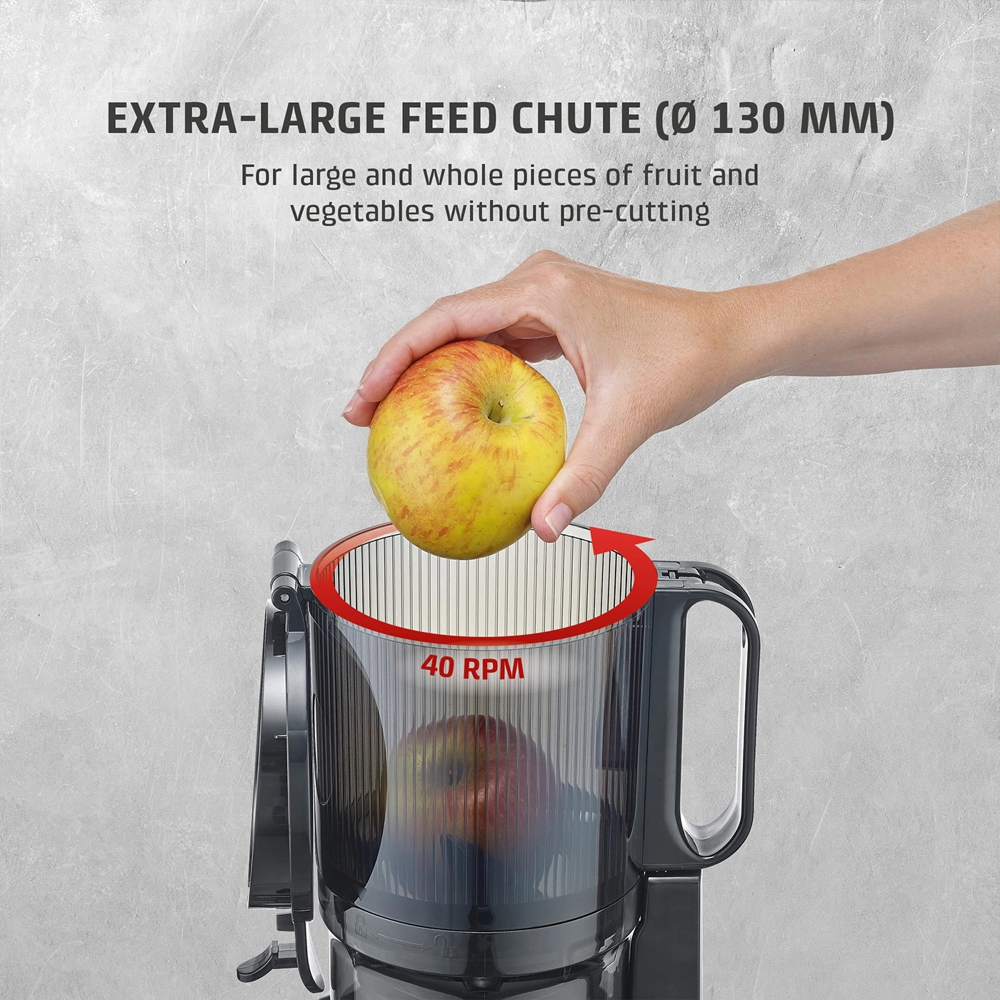 A hand places an apple into a large juicer opening.