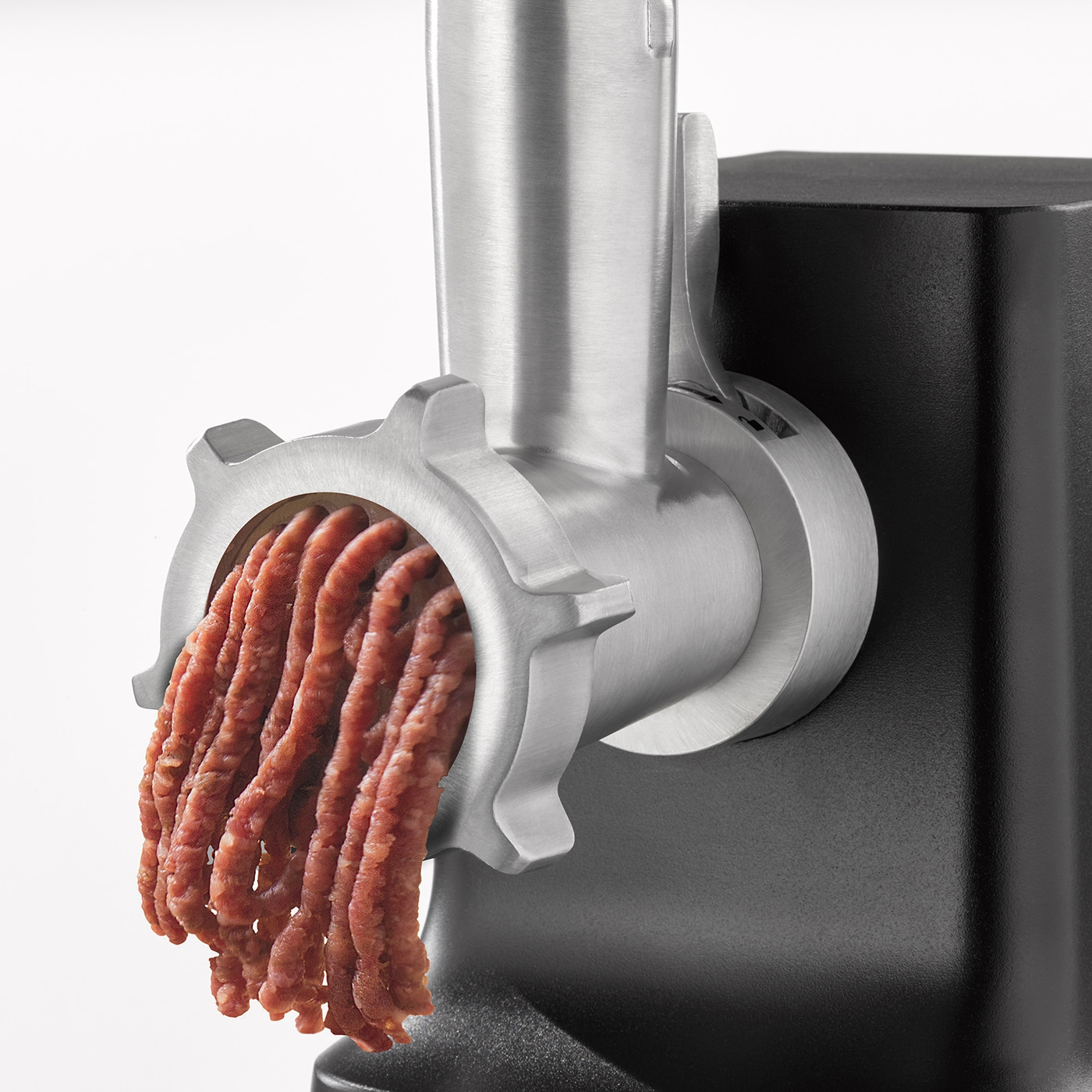 Nahaufnahme eines Fleischwolfs, der Fleisch ausgibt, mit schwarzem Hintergrund und hellem Licht